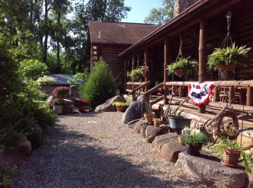 A scenic pathway lined with potted plants and flowers, leading to a rustic log cabin surrounded by trees.
