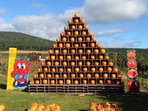 A pyramid of stacked pumpkins on wooden pallets, with colorful cartoon characters and a scenic background.