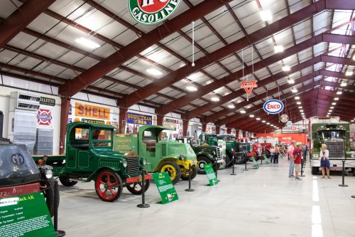 A vintage vehicle museum showcasing classic trucks and gas station signs in a spacious indoor setting.