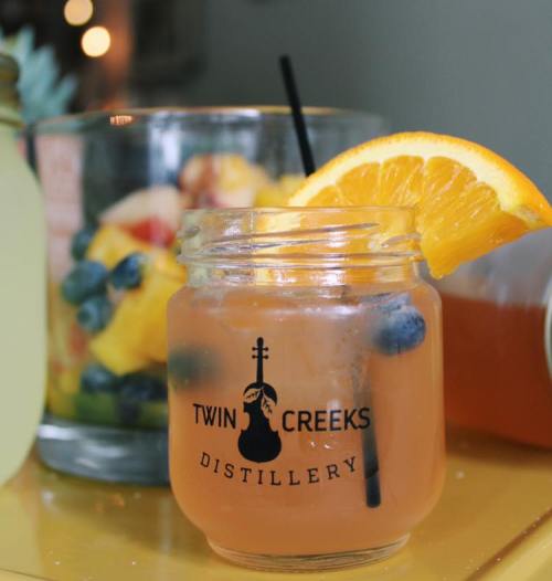 A refreshing cocktail in a jar with an orange slice and blueberries, next to a fruit-filled jar.