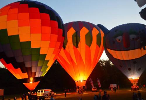 Three brightly colored hot air balloons illuminated at dusk, with vibrant patterns and a playful face on one balloon.