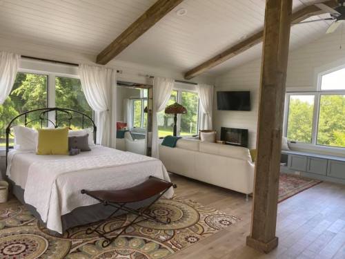 Bright, airy bedroom with a bed, sofa, large windows, and wooden beams, overlooking a green landscape.