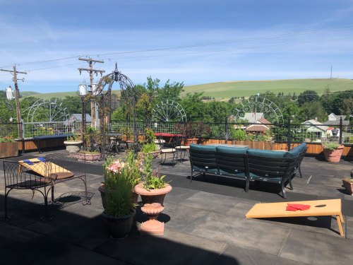 A rooftop patio with seating, planters, and a view of green hills and blue sky.