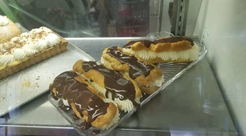 A display of eclairs topped with chocolate glaze and filled with cream, set in a glass case.
