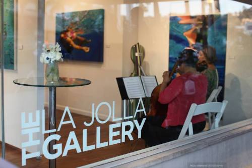 A view of the La Jolla Gallery with musicians performing inside, surrounded by colorful artwork.