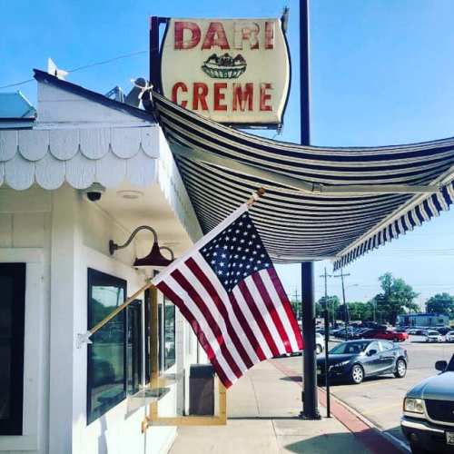 A vintage sign for "Dari Creme" with an American flag hanging outside a charming building on a sunny day.