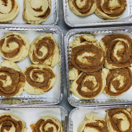 Freshly made cinnamon rolls arranged in aluminum trays, showcasing their swirled, cinnamon-filled dough.
