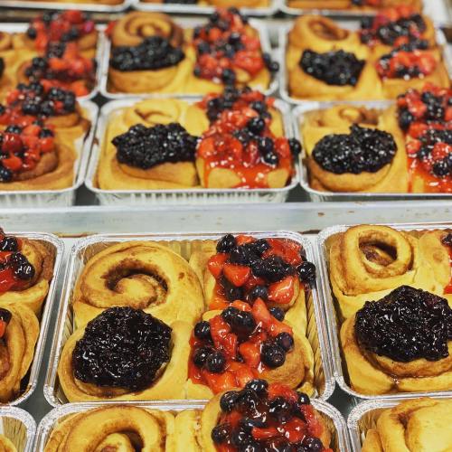 Freshly baked cinnamon rolls topped with vibrant berry compote in aluminum trays.