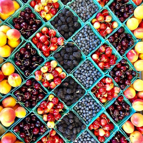 A colorful arrangement of various fruits in small containers, including cherries, blueberries, blackberries, and peaches.