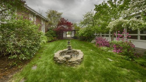 Lush garden with a stone fountain, surrounded by vibrant flowers and greenery, under a cloudy sky.