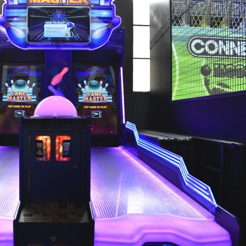 A colorful arcade game machine with a glowing interface and screens, set in a vibrant gaming environment.