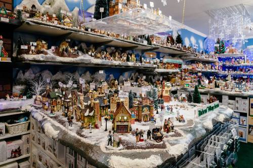 A festive display of miniature houses and figures on a snowy landscape, surrounded by holiday decorations.