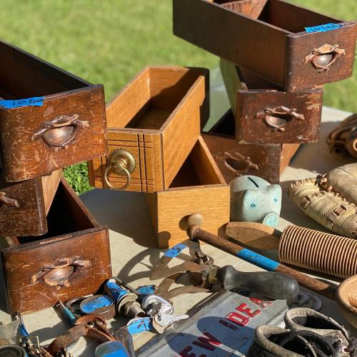 A collection of vintage wooden drawers and assorted tools arranged on a table outdoors.