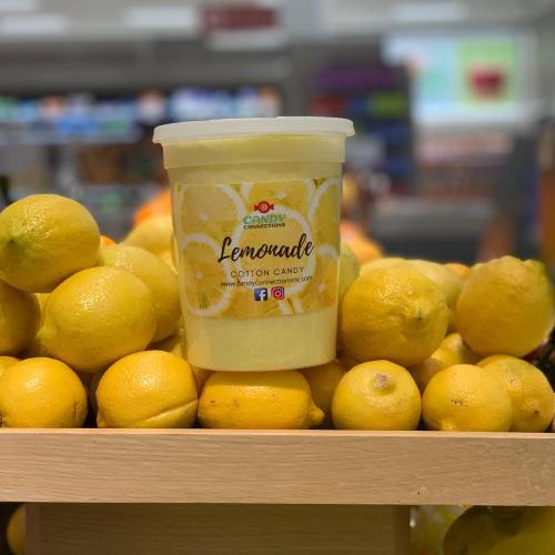 A container of lemonade-flavored cotton candy sits atop a pile of fresh lemons in a store display.
