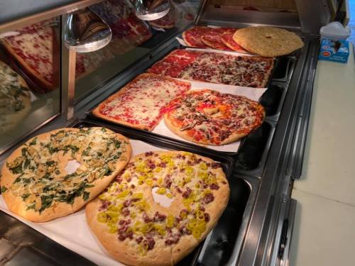 A variety of pizzas displayed in a food counter, including cheese, pepperoni, and specialty toppings.