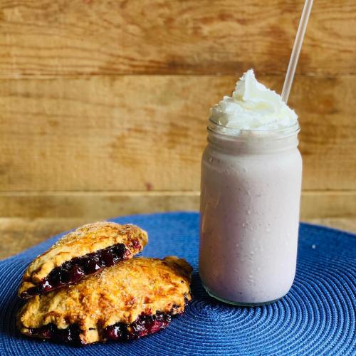 A mason jar filled with a creamy smoothie topped with whipped cream, next to two flaky berry-filled pastries.