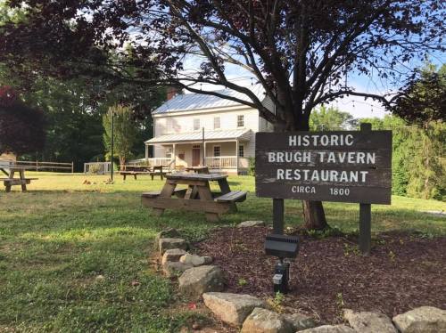 Historic Brugh Tavern Restaurant sign in front of a white building, surrounded by trees and picnic tables. Circa 1800.