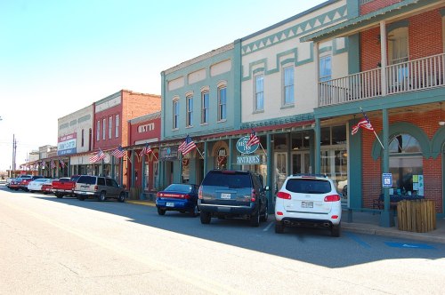 A charming small-town street lined with historic buildings and American flags, featuring parked cars along the curb.