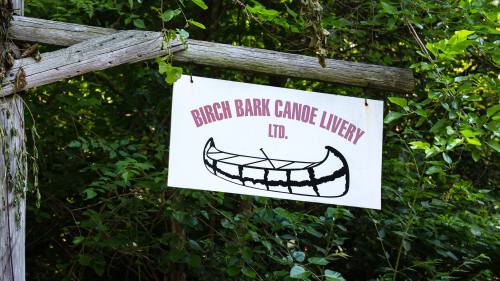 Sign for Birgh Bark Canoe Livery, featuring a canoe illustration, surrounded by lush greenery.