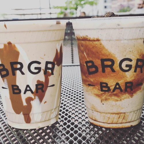 Two cups of milkshakes with chocolate and vanilla swirls, featuring the logo "BRGR BAR" on a textured surface.