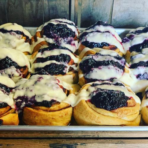 A tray of freshly baked cinnamon rolls topped with creamy icing and blueberry filling.