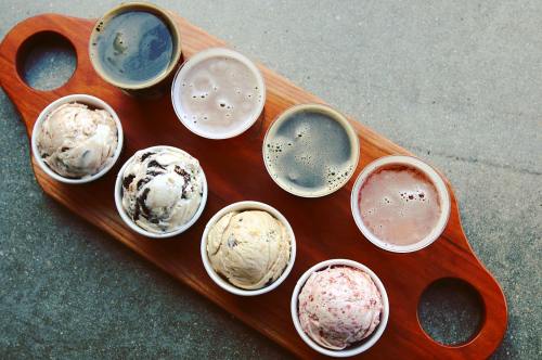 A wooden tray holds eight cups of ice cream and beer, arranged in two rows, showcasing various flavors and colors.