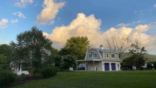 A charming white house with purple doors, surrounded by green grass and trees, under a blue sky with fluffy clouds.