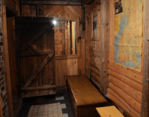 A rustic wooden room featuring a door, a mirror, a map on the wall, and a wooden bench.