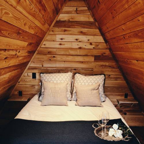 Cozy bedroom with wooden walls, a double bed with decorative pillows, and a small table set with glasses and flowers.