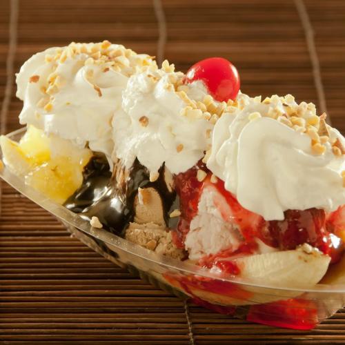 A colorful banana split topped with whipped cream, nuts, cherries, and various sauces on a wooden surface.