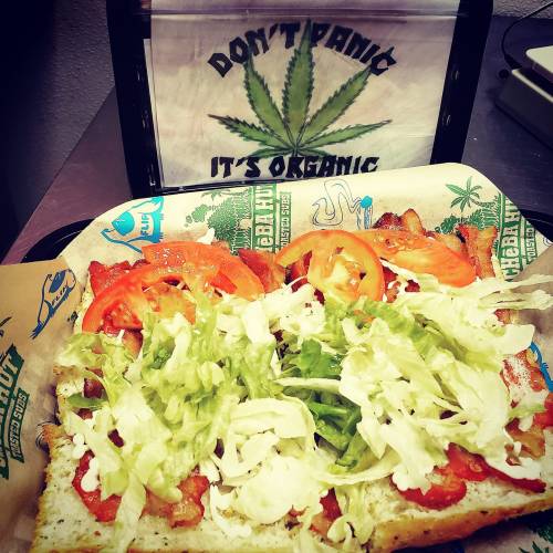 A sandwich topped with lettuce, tomatoes, and bacon, next to a sign that says "Don't Panic, It's Organic."