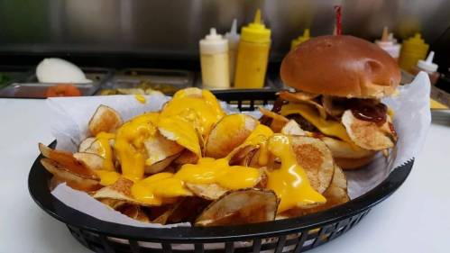 A basket of cheesy potato chips alongside a burger with a soft bun and toppings.