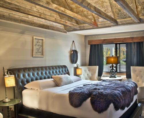Cozy bedroom with a tufted bed, wooden beams, and stylish decor, featuring a fur throw and soft lighting.