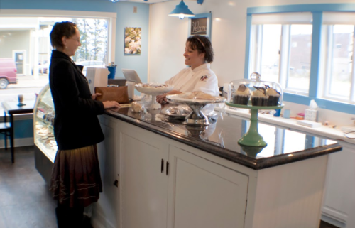 A customer interacts with a staff member at a bakery counter, surrounded by baked goods and a bright, inviting atmosphere.
