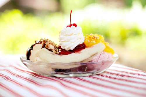 A banana split sundae with whipped cream, cherry on top, and various toppings in a glass dish on a striped tablecloth.