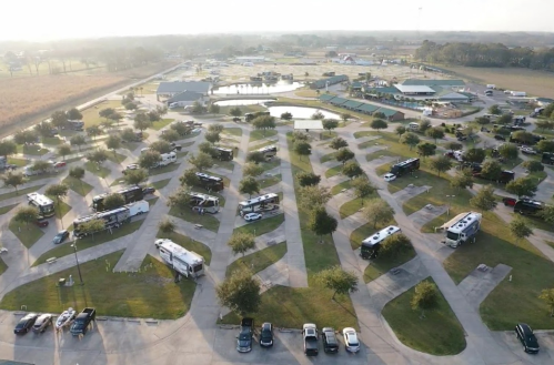 Aerial view of a spacious RV park with numerous parked RVs, surrounded by green lawns and a pond.
