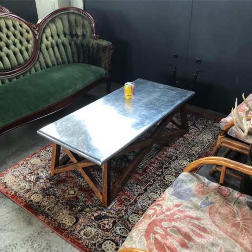 A green velvet sofa and a wooden coffee table with a metal top, set on a patterned rug in a cozy room.
