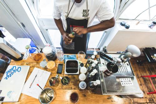 A barista prepares a drink at a coffee shop, surrounded by various tools and ingredients on a wooden counter.