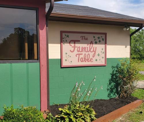 Sign for "The Family Table" on a building, featuring green and maroon colors with decorative ivy accents.