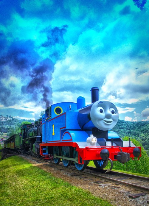 A cheerful blue train with a smiling face, chugging along a green landscape under a vibrant sky.