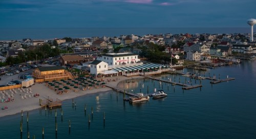 Aerial view of a beachside town at dusk, featuring a restaurant, docks, and residential buildings along the shore.