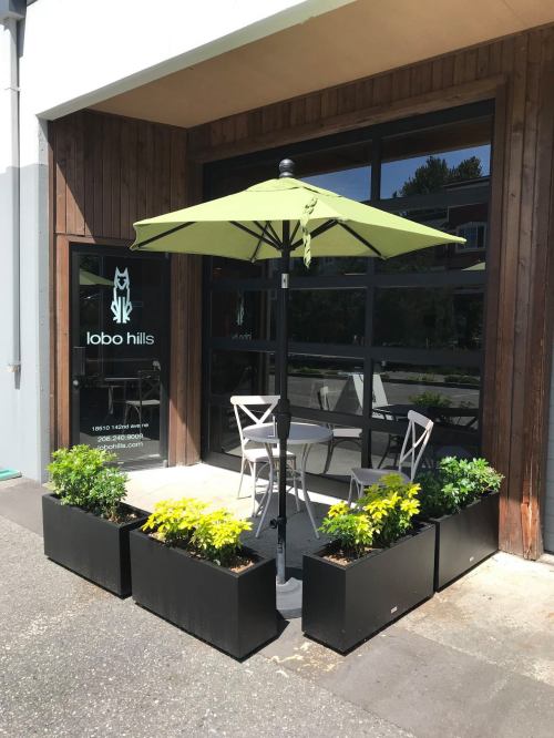 A small outdoor seating area with a green umbrella, two chairs, and planters outside a building with "lobo hills" signage.