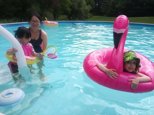 A woman and two children play in a pool, one child in a pink flamingo float and the other holding a toy.