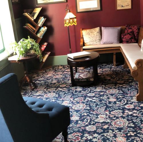Cozy reading nook with a blue chair, a small table, a plant, and a bookshelf against a deep red wall.