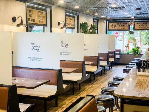 A cozy diner interior with booths separated by partitions, featuring a counter and large windows.