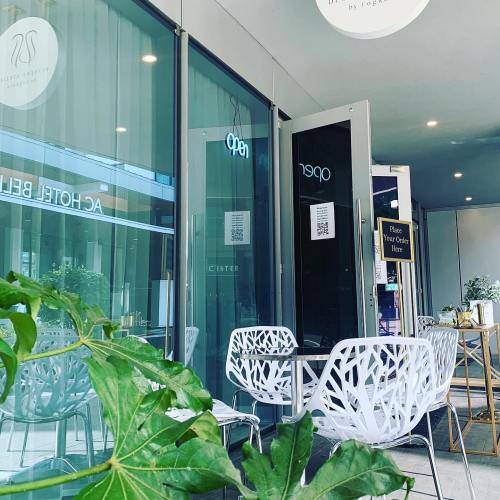 A modern café entrance with glass doors, white chairs, and plants, inviting customers to place their orders.