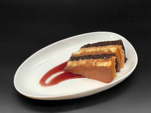 A slice of layered chocolate and vanilla cake on a white plate, drizzled with red sauce.