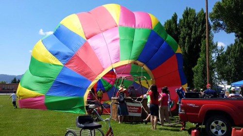 A colorful hot air balloon is being prepared on a grassy field, with people gathered around and trees in the background.