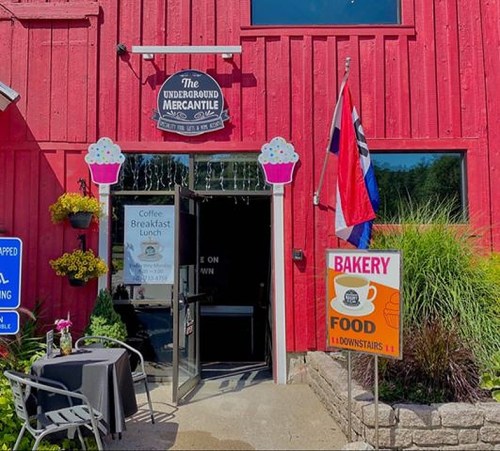 Entrance of The Underground Mercantile, featuring a red wooden exterior, bakery sign, and colorful decorations.
