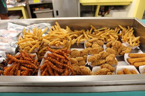 A metal tray filled with various fried foods, including crinkle-cut fries, chicken tenders, and sweet potato fries.